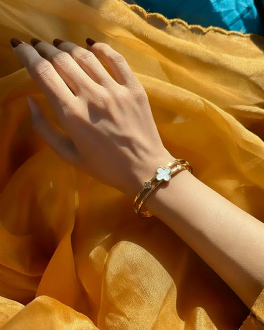Hand wearing a gold bracelet on a yellow fabric background