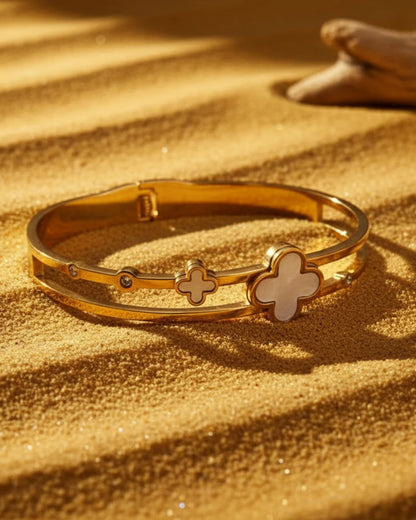 Gold bracelet with clover designs on a sandy background